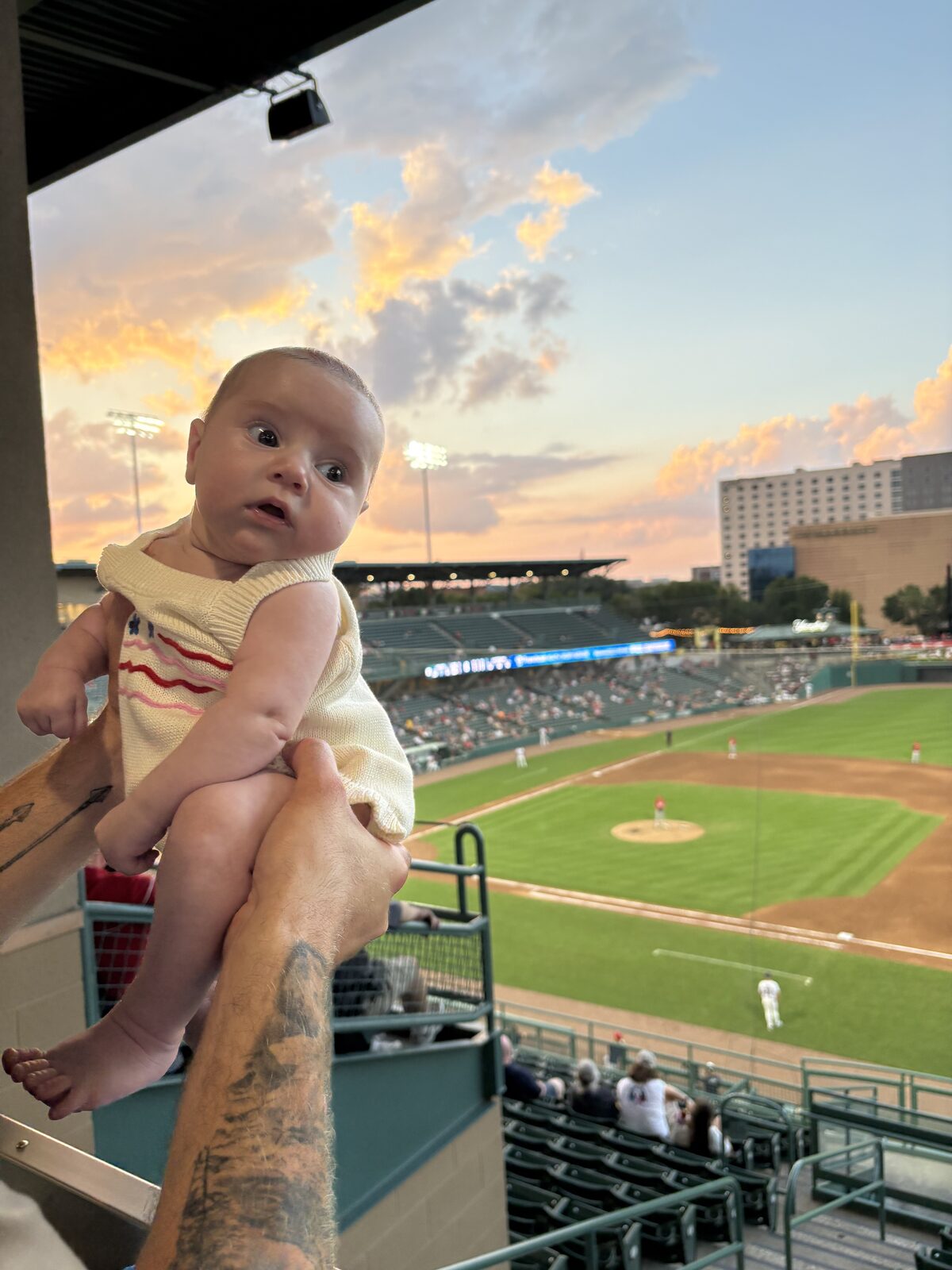 Gabe holding his newborn daughter at a baseball game
